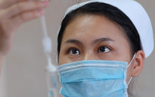 佩戴醫(yī)用口罩的護(hù)士給患者輸液